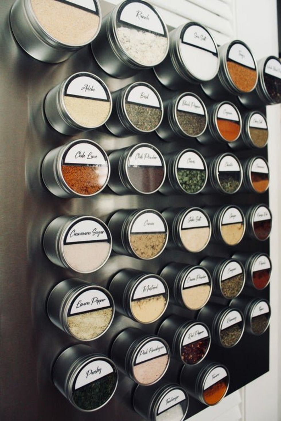 Spices in round metal containers stuck to a magnetic sheet on the wall.