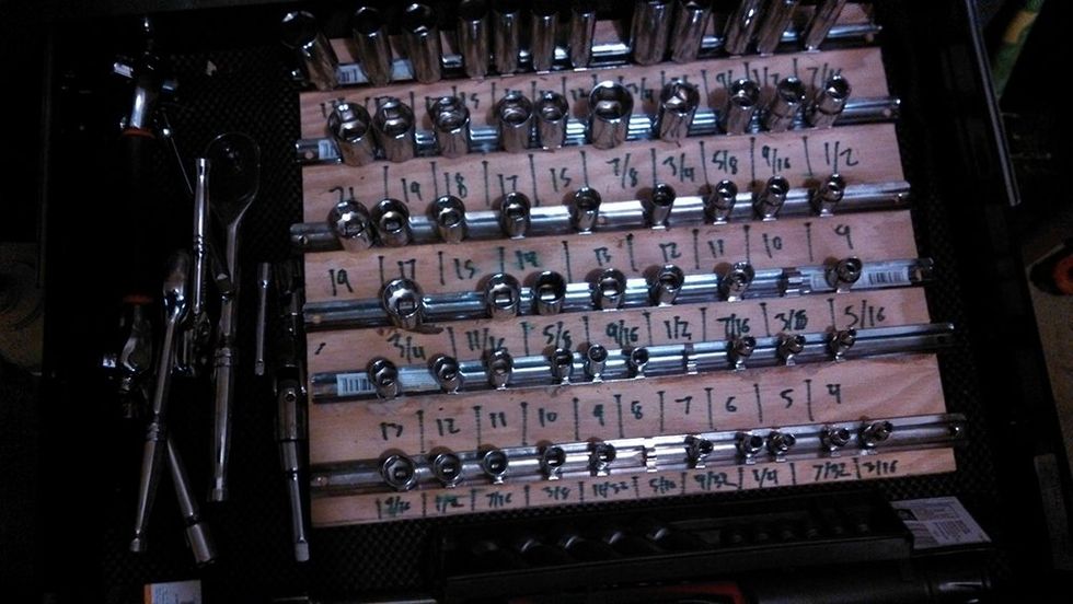 Magnetic strips stuck to a piece of plywood. Along each one are lug nuts. Under each lug nut the size is written in marker