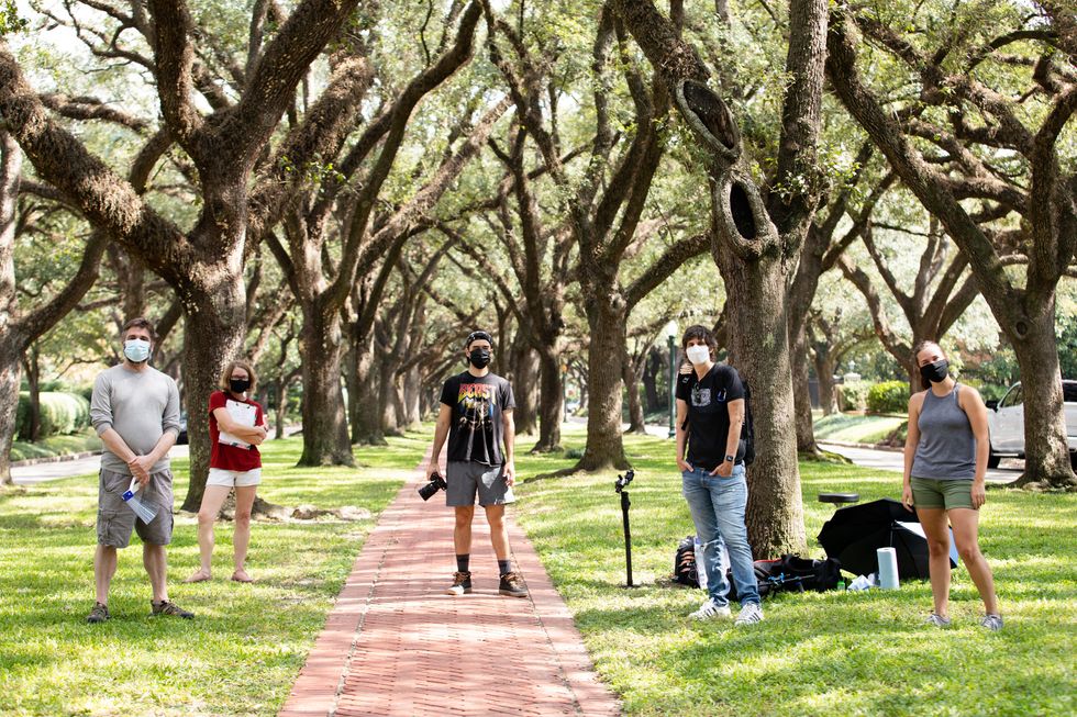 Three men and two women in casual street clothes stand under a grove of oak trees, surrounded by camera equipment.