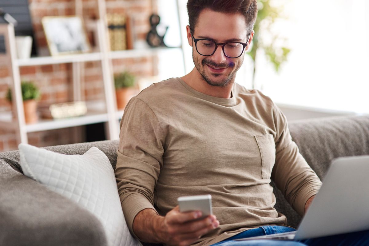 man sitting on couch looks at his phone and smiles