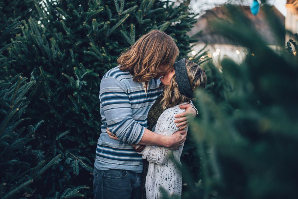 man kissing woman near pine tree