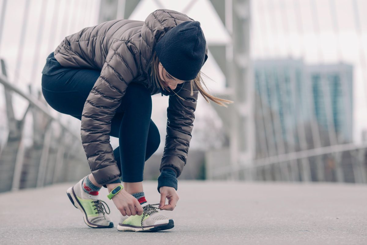 Woman on a bridge, tying her shoe for a run. 