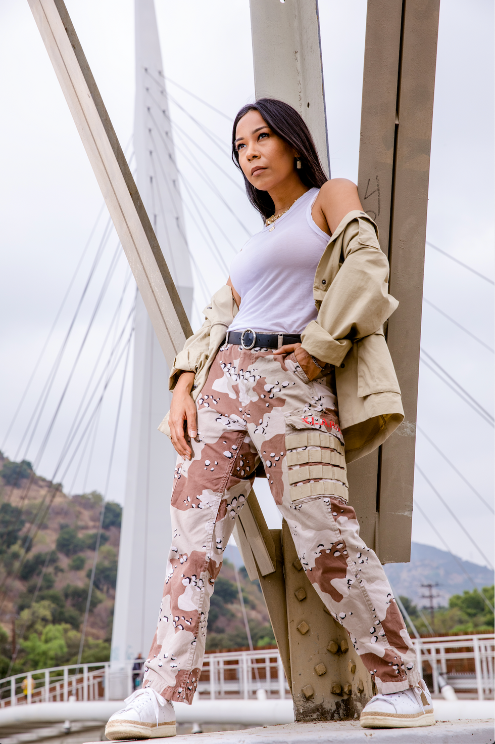 Bridges frame Galen Hooks in the background as she stands with feet wide apart, some California hills behind them