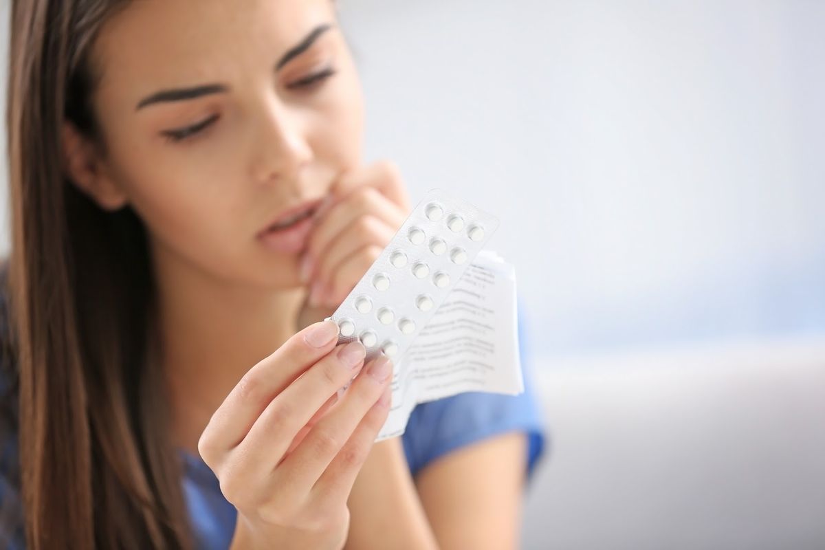 woman with brown hair holding birth control pills and reading the leaflet