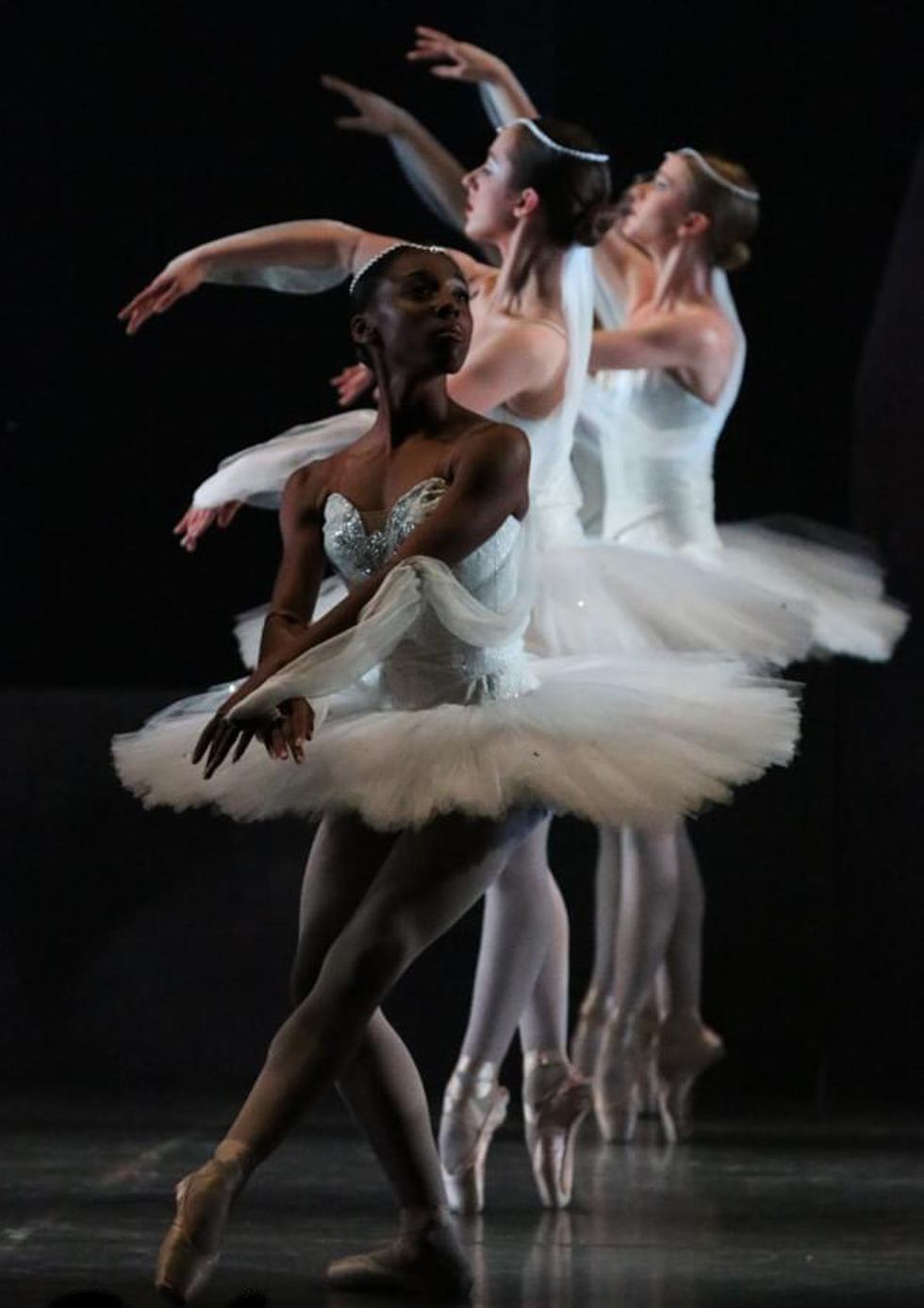 Aerys Merrill is at the front of a line of dancers in classical white tutus and pointe shoes. She is in pli\u00e9 tendu devant while the dancers behind her stand in sous-sus.