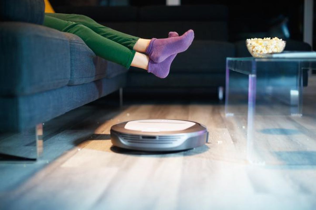 A robot vacuum rolling under someone's feet in front of a couch