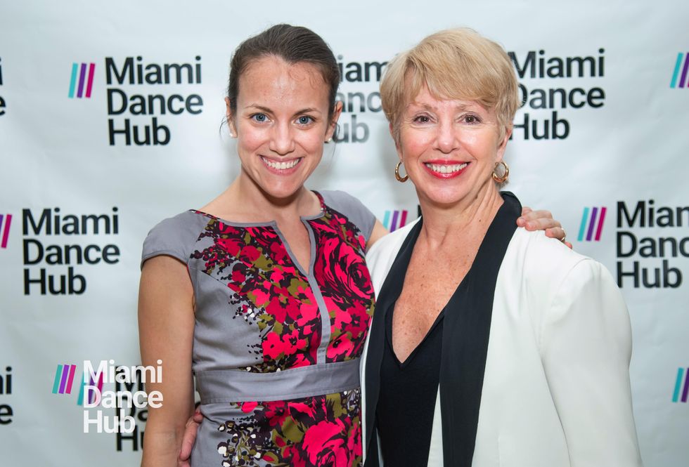Two women in gala clothes stand in front of a backdrop that repeats thee phrase Miami Dance Hub