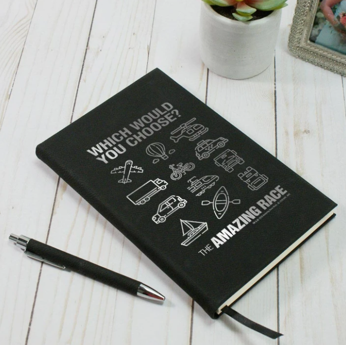 Black faux leather journal with The Amazing Race logo and transportation icons