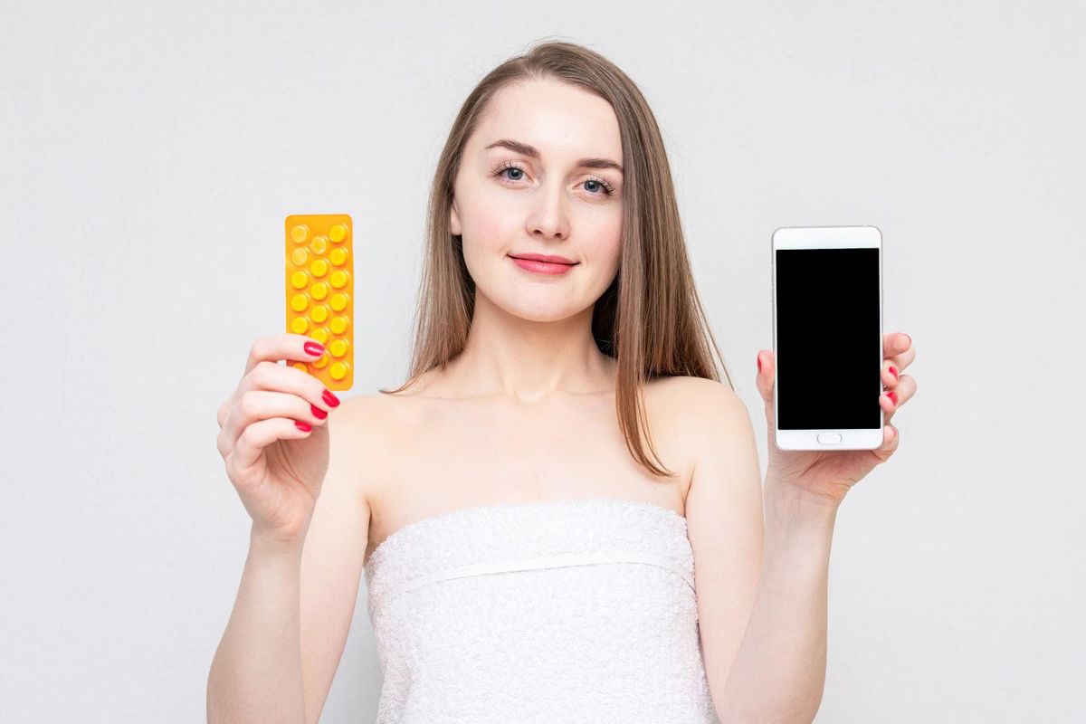 Woman holding Nurx birth control and cell phone.