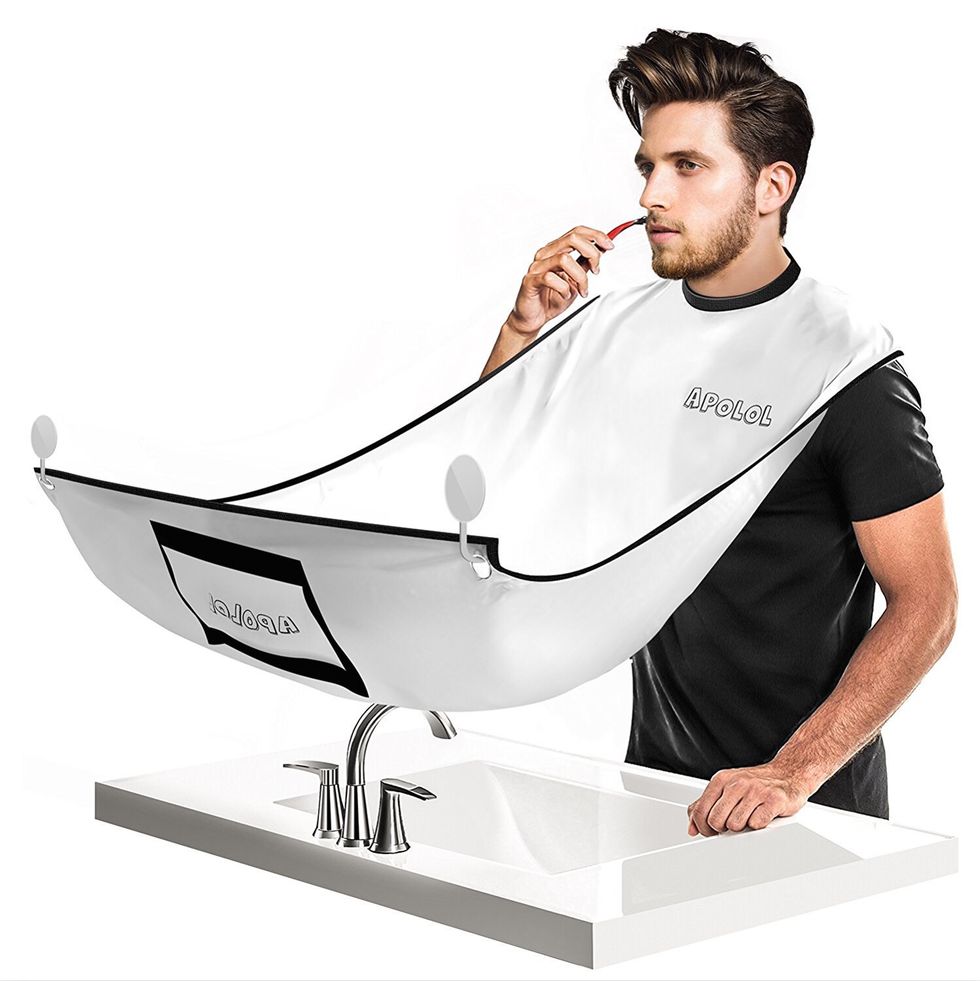 A man shaves a bear with a sheet around his neck to catch the bear trimmings.