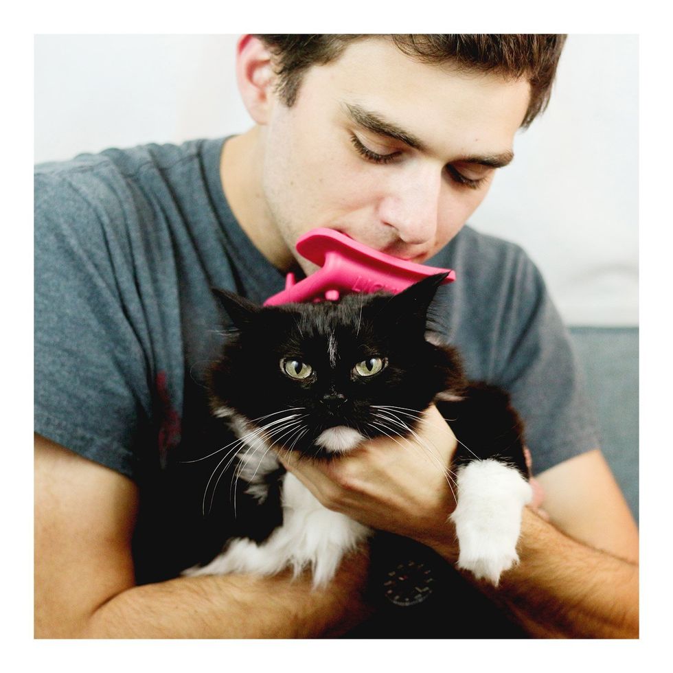 A man with a cat brush in his mouth that allows him to lick the cat in his lap.