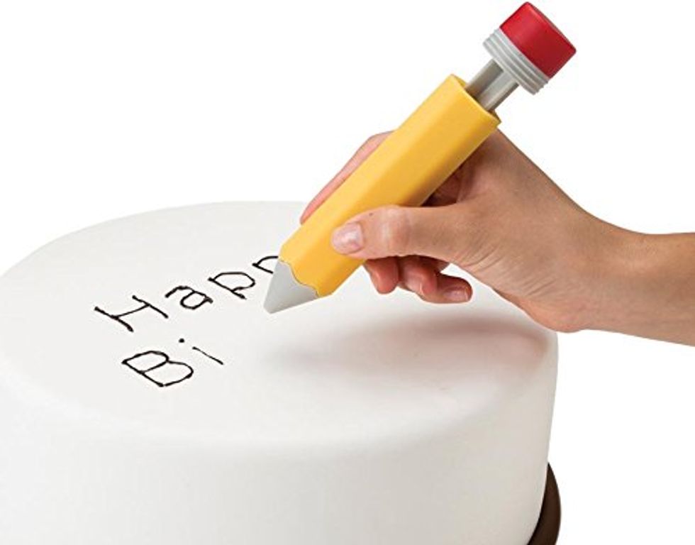 A cake decorating tool in the shape of a pen that is writing out happy birthday on a cake.