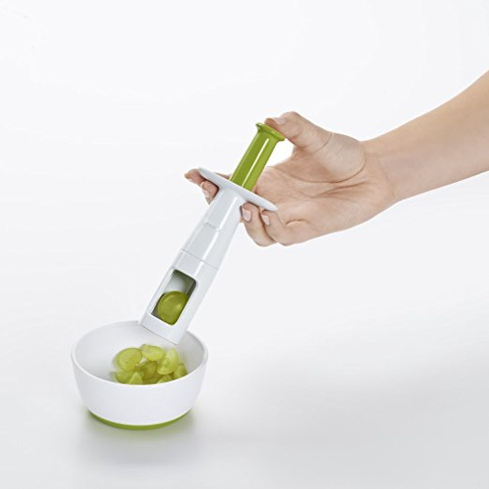 A person uses a grape slicer to slice grapes into a bowl.