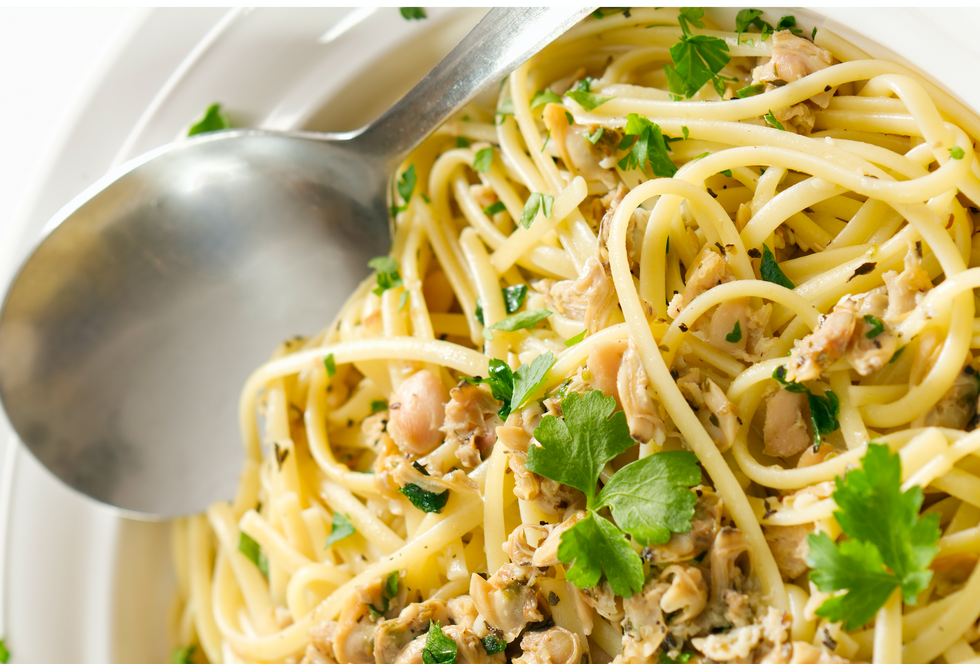 A close photo of white plate with linguine pasta, clams and parsley