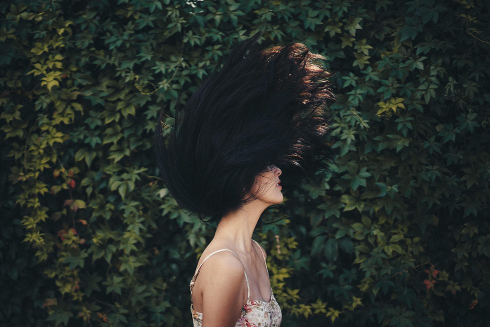 Woman flipping her hair in front of a wall of leaves