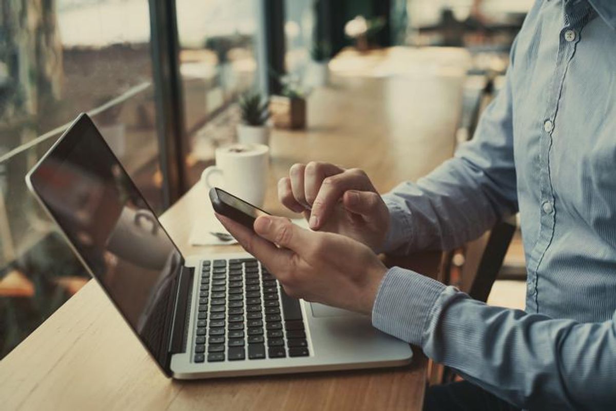 Man holding a smartphone with a laptop in front of him