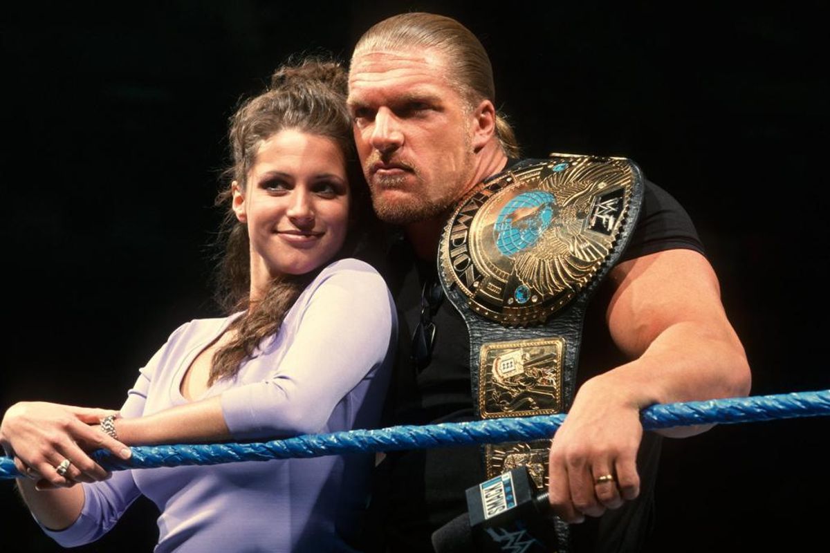 Stephanie McMahon smiling next to Triple H while he looks serious in the ring