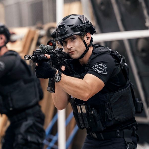 A SWAT team membemr wears a helmet with the visor down as he points a gun during a tactical advance.
