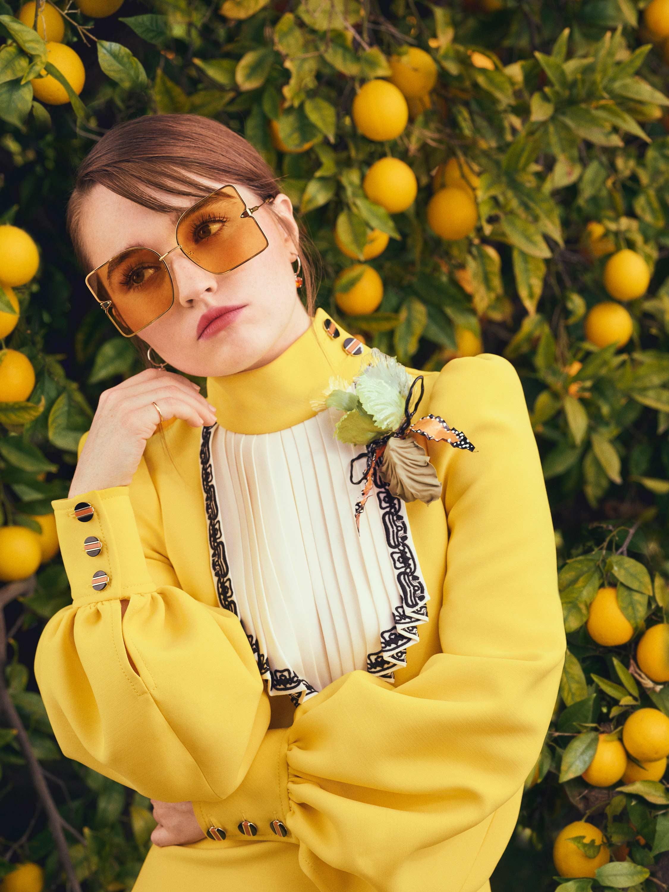 Kaitlyn Dever sports a bright yellow dress with a high collar and a pleated white bib front