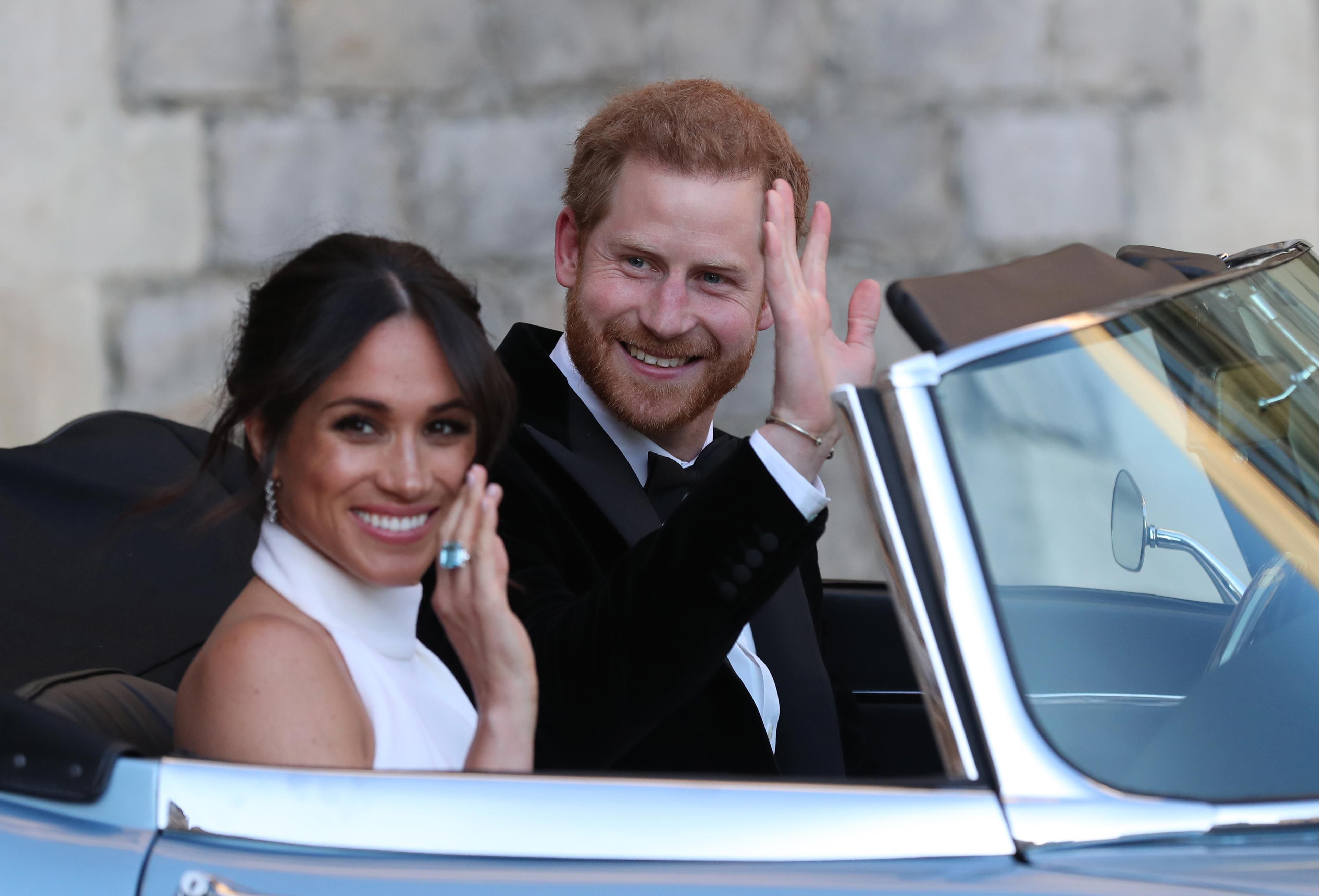 Harry and Meghan wave from the front seat of a convertible