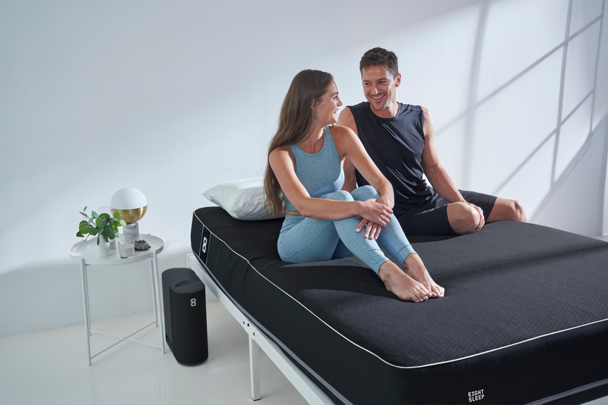 A couple sitting on an Eight Sleep Pod Pro mattress