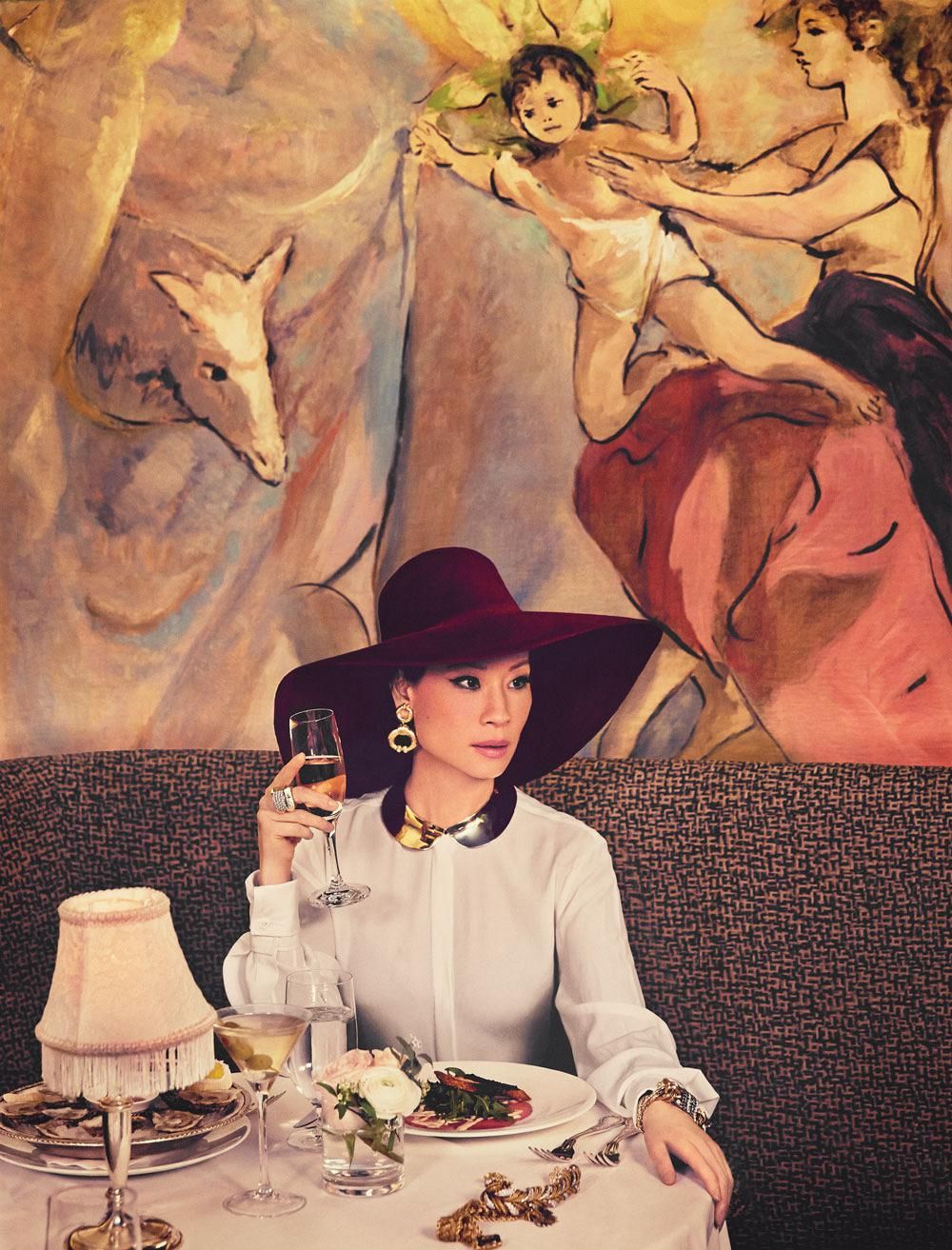 Lucy Liu poses in a restaurant booth in a dramatic burgundy hat