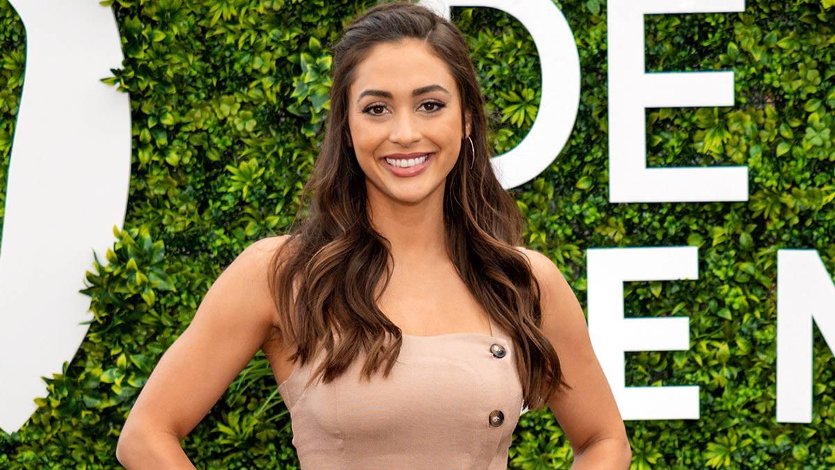 Actresss Lindsey Morgan smiles and poses on a red carpet photoshoot in front of greenery.