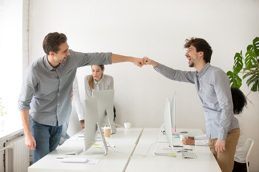 Two coworkers celebrate their office pool success with a fist bump.