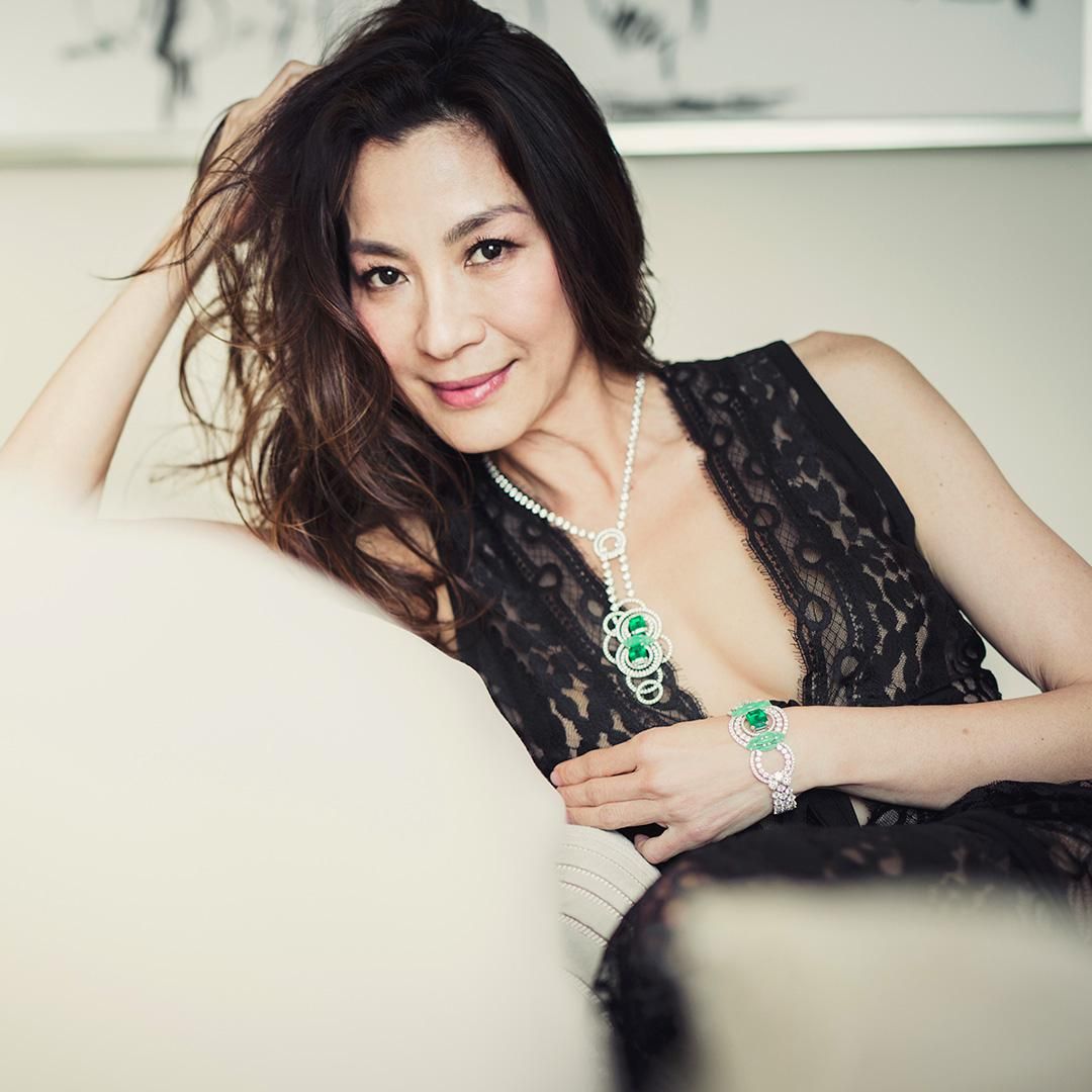 Michelle Yeoh in a lacy black top and diamond and emerald jewelry.