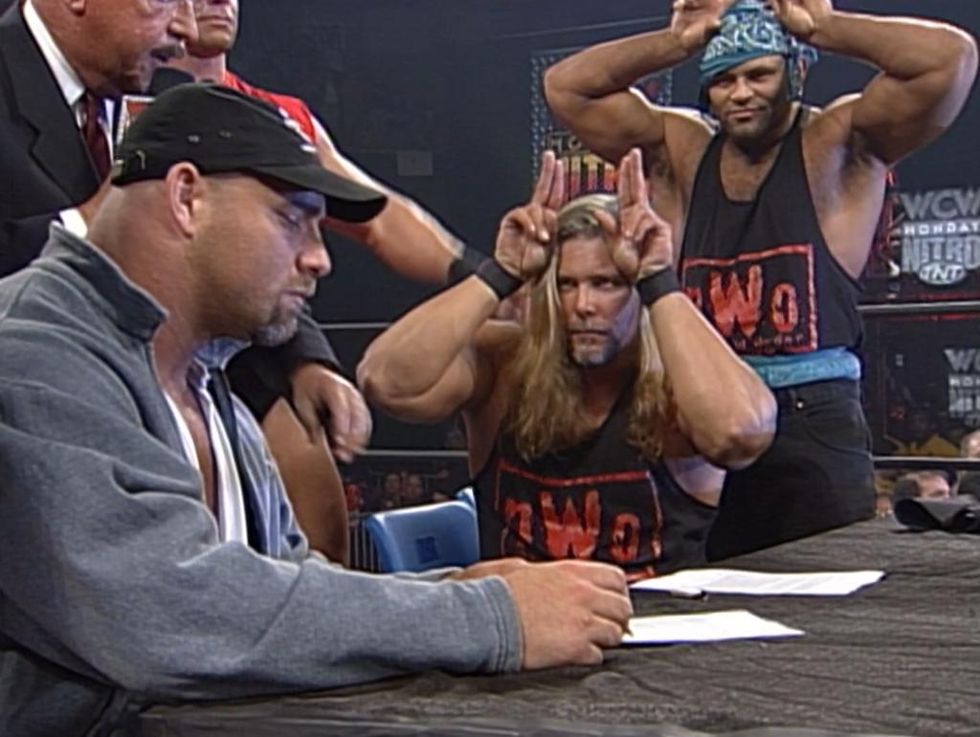 Kevin Nash and Konnan holding up wolf ears as Goldberg signs a contract