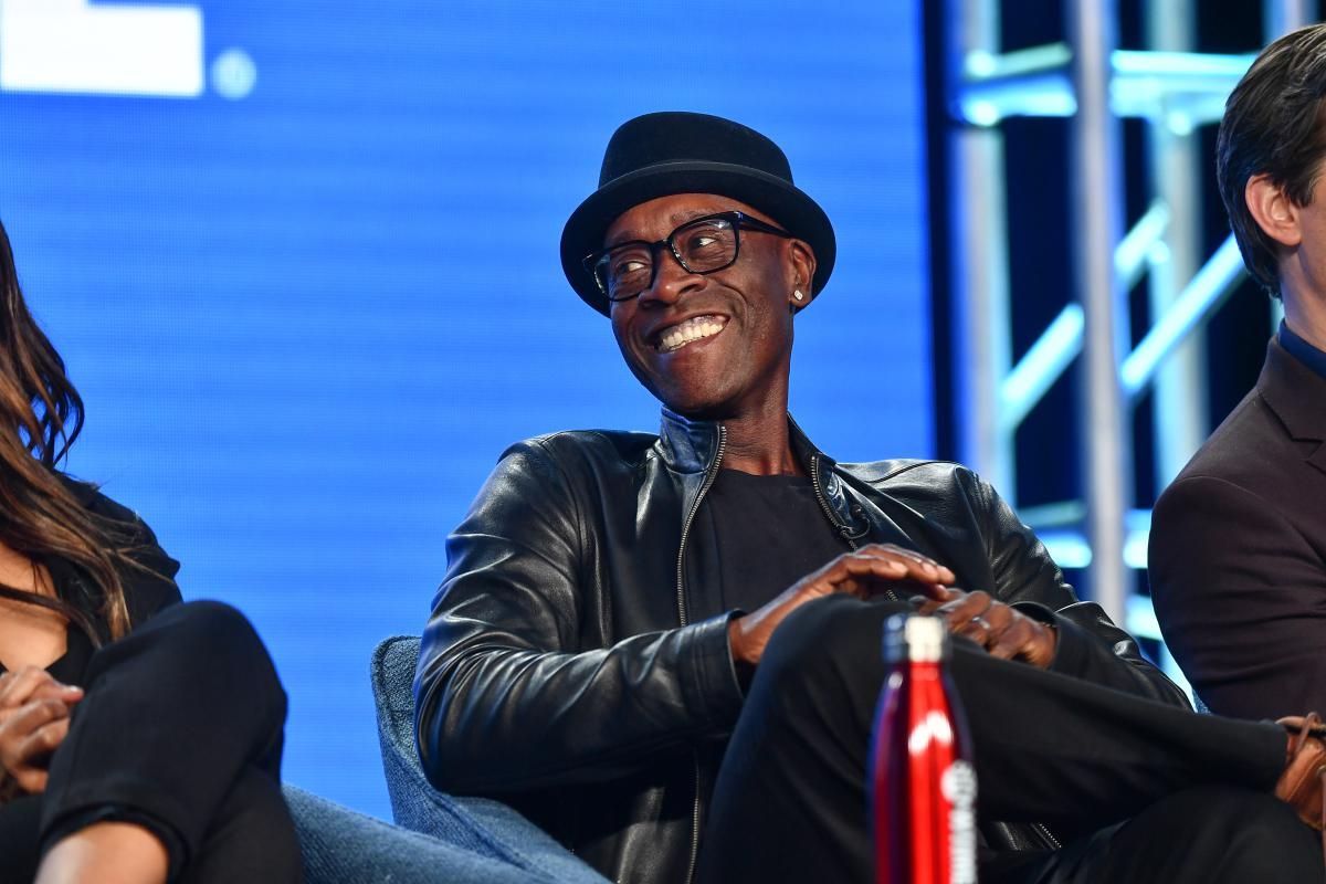 Don Cheadle wearing a hat and smiling during a press tour