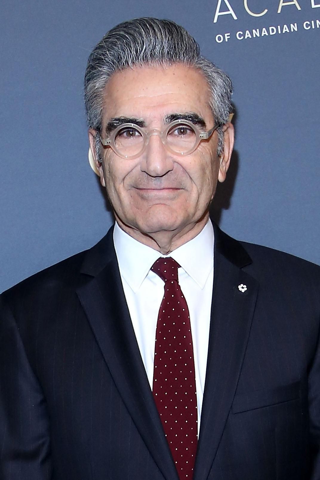 Eugene Levy in a suit and clear glasses