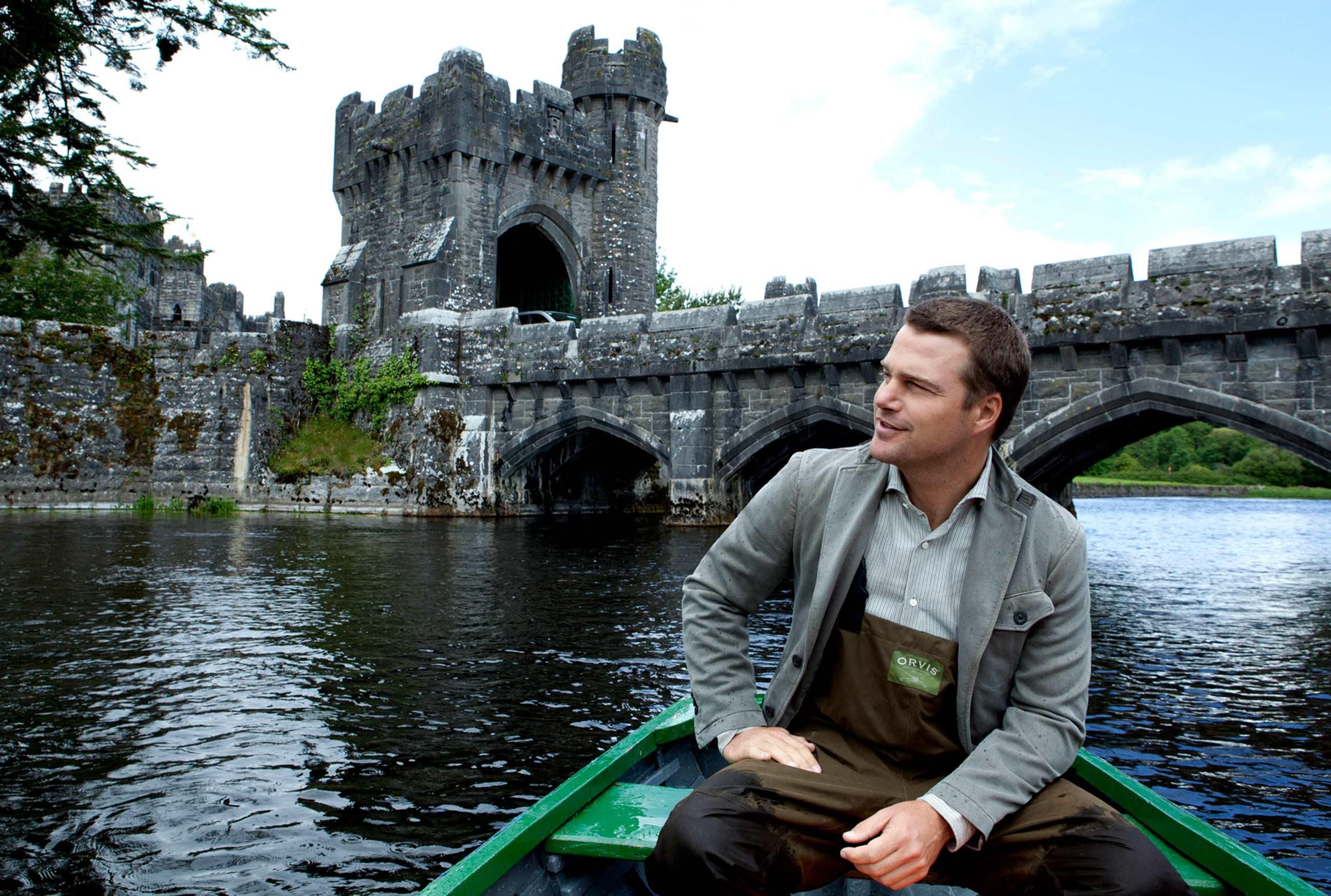 Chris O'Donnell in a row boat with a castle behind him.