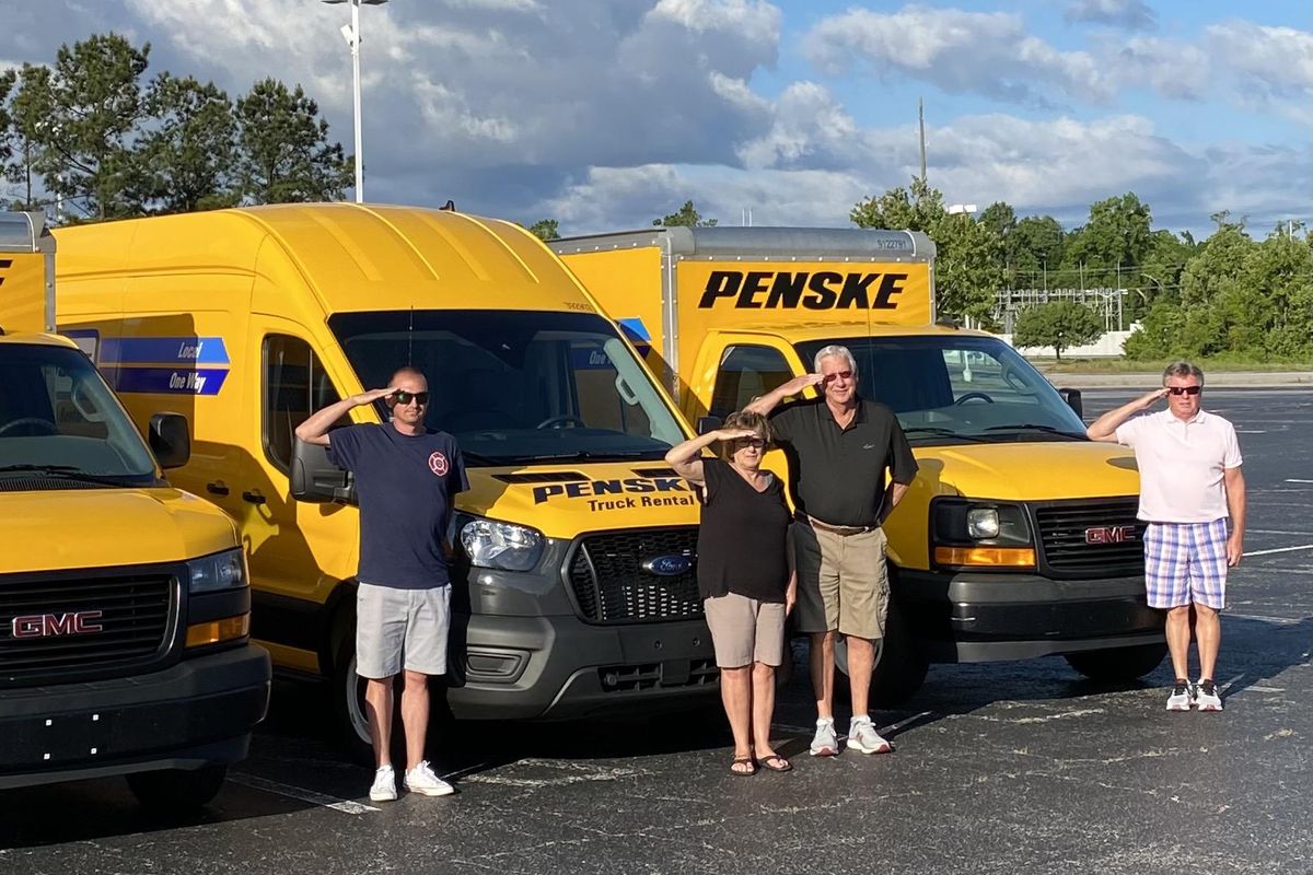 military family saluting in front of penske trucks