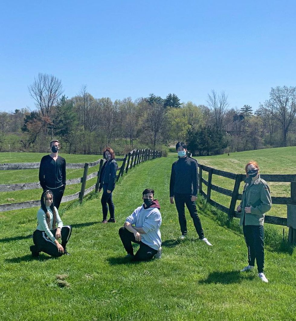 A group of six people\u2014three men and three women\u2014pose on a grassy field between two wooden fences, posing in jackets and assorted athleisure.