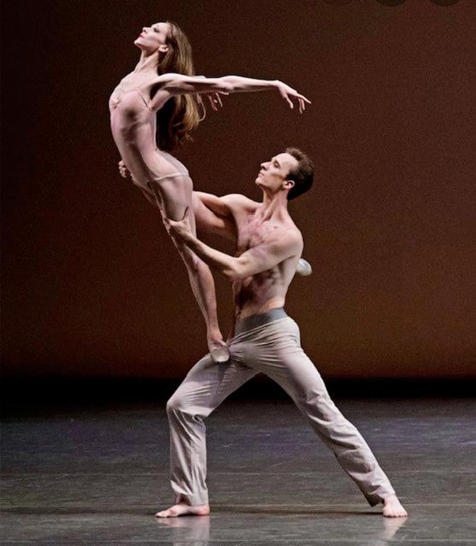 Ask la Cour lunges forward while Maria Kowroski stands on his right thigh. Her right leg reaches behind his right side in a low arabesque and she arches back slightly wit her arms outstretched. Her brown hair is long and flowing, and she wears a pink leotard, while he wears off-white pants.