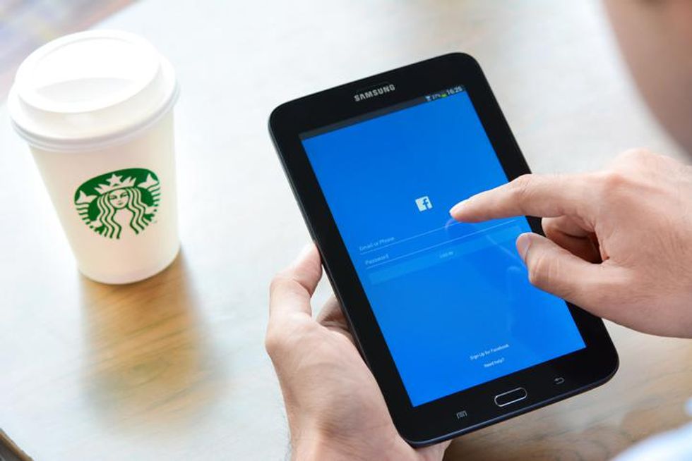 Person holding a Samsung tablet while logging into facebook with Starbucks coffee cup