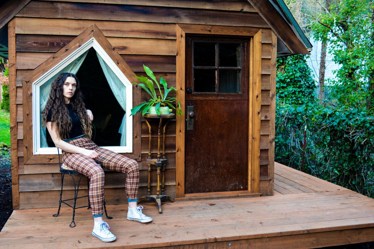 Singer-songwriter and guitarist Jessie Antonick sits in front of a cabin she built for herself.