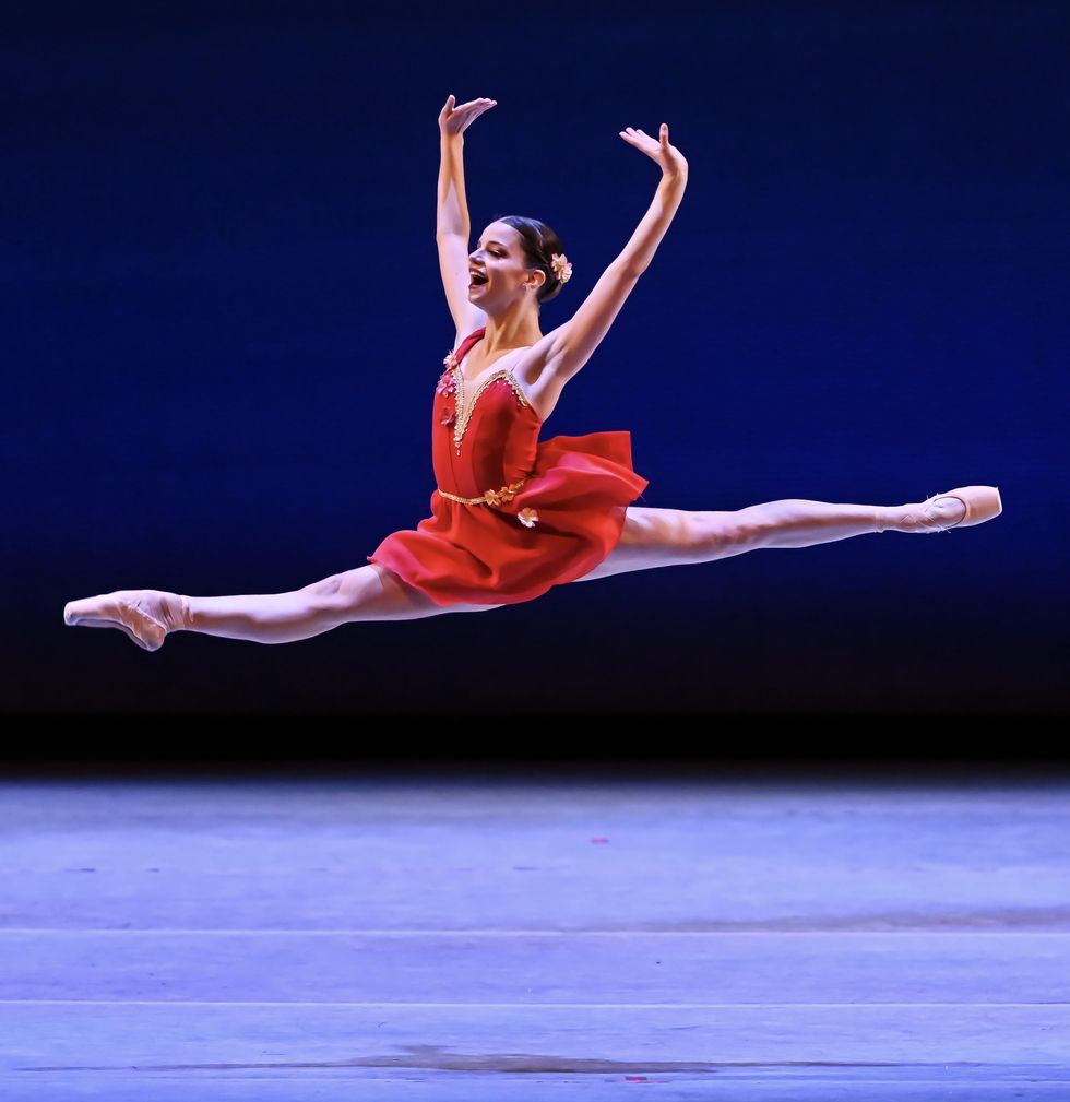 Clara Thiele soars through the air in a grand jet\u00e9 above the stage, mouth wide open, hands flexed above her head.