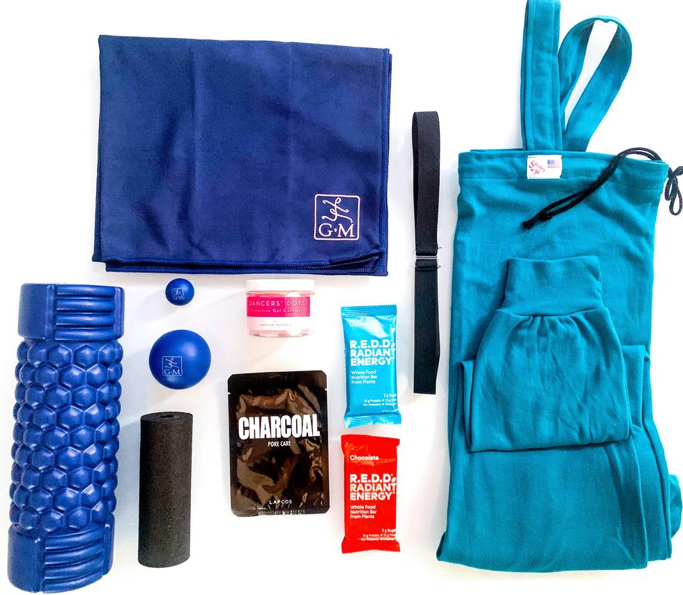 A foam roller, energy barres, elastic waistband and teal warm-up jumper are neatly organized on a white background and photographed from above.