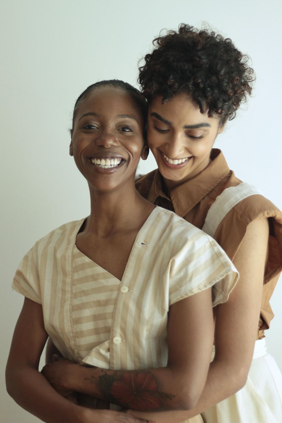 Audrey Malek, wearing a brown shirt, stands behind Cortney Taylor-Key and wraps her around her waist. Taylor-Key holds onto Malek's arms, and both dancers wear large, joyful smiles.