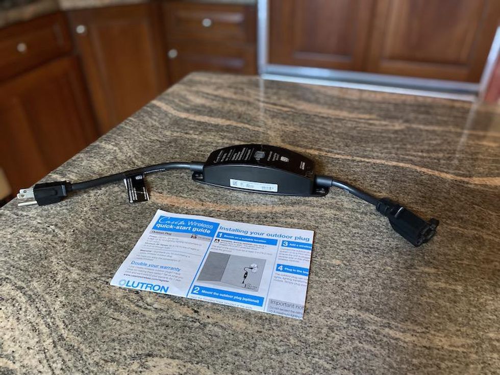 Lutron Caseta Outdoor Smart Plug on a countertop with Quick Start Guide