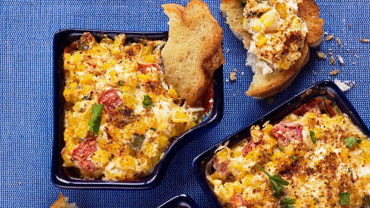 Creamy corn dip in bowls on blue tablecloth with crusty bread at side