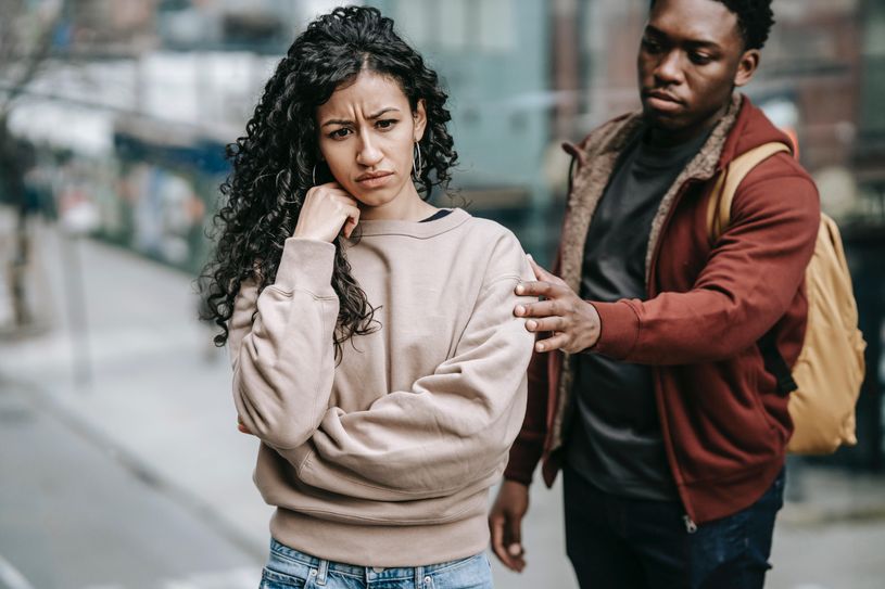 man trying to talk to woman by putting hand on her shoulder