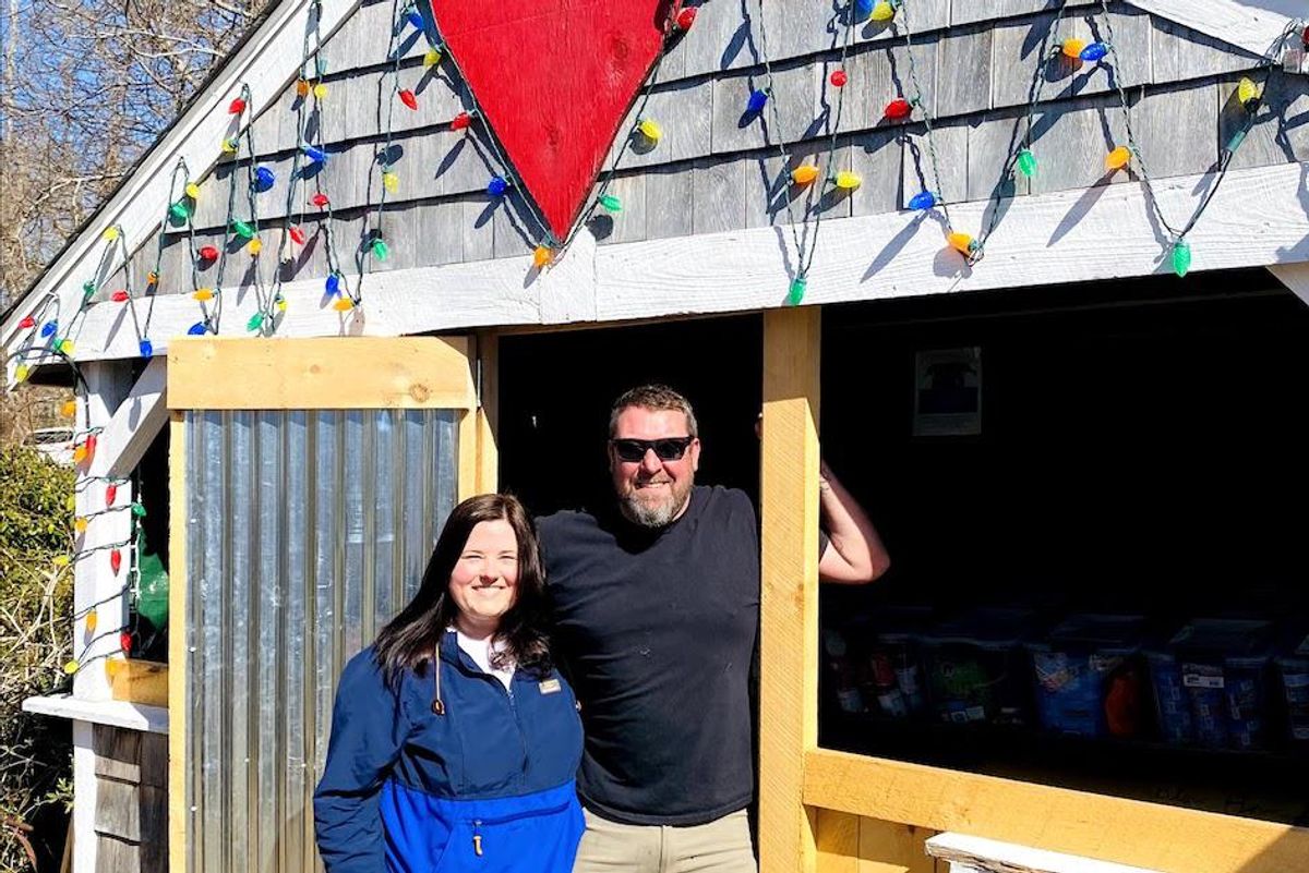 A man and woman, smiling, stand in front of a farm stand