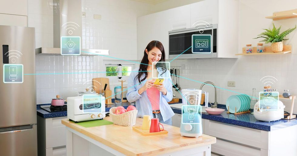 A photo of a kitchen with smart appliances controlled by a woman and an app on a smartphone.
