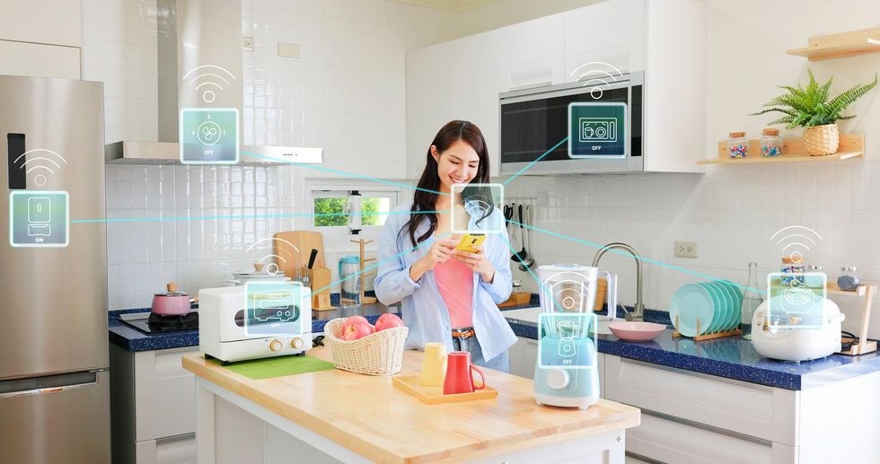 a photo of a kitchen with smart appliances being controlled by a woman and an app on a smartphone.