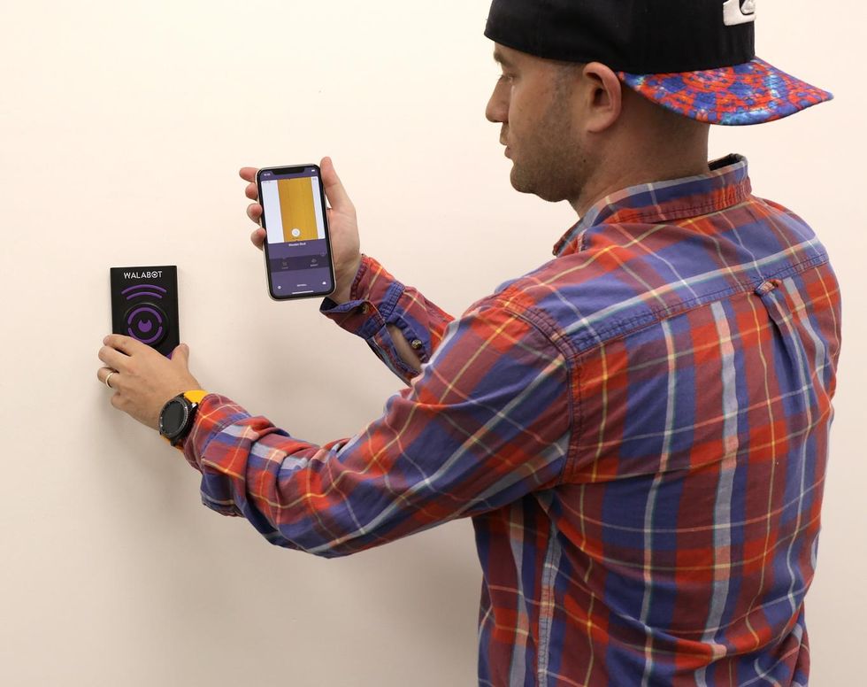 A person using Walabot DIY 2 on a wall to locate studs or pipes behind the wall