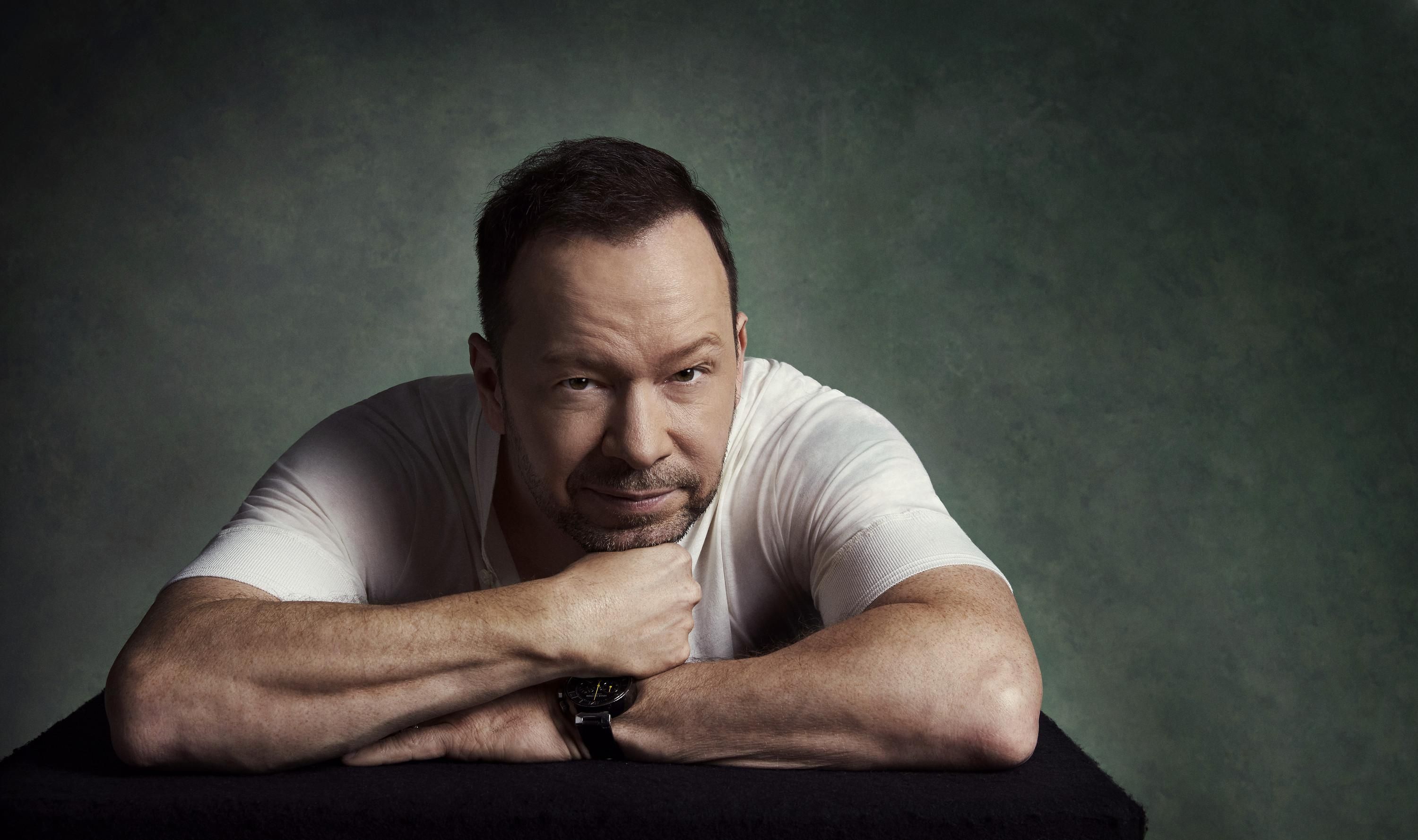 Donnie Wahlberg wearing a white T-shirt and leaning on his elbows staring at the camera