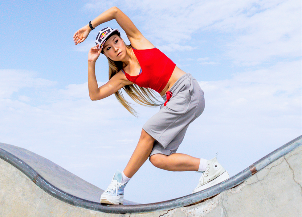 Dassy Lee looks under her arm balancing on a curved structure against a blue sky